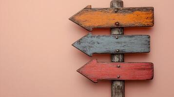 Rustic wooden direction signs in orange, red, and gray colors mounted on weathered, photographed against light peach background in minimalist modern composition. photo
