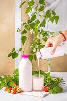 Woman pouring strawberry yogurt into glass with fresh strawberries and mint photo