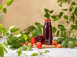 Fresh strawberry juice in glass bottles surrounded by strawberry leaves photo