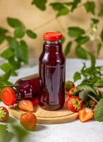 Two strawberry juice bottles standing on wooden board with fresh strawberries and leaves photo