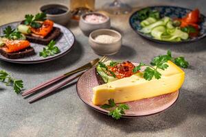 Wedge of cheese with sandwiches topped with smoked salmon and cucumber on gray table photo
