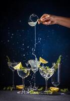 Bartender pouring gin into cocktail glasses with lemon and juniper berries, creating splashing effect photo