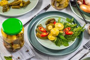 Pickled pattypan squash, cucumbers and chili pepper with fresh herbs on green plate photo