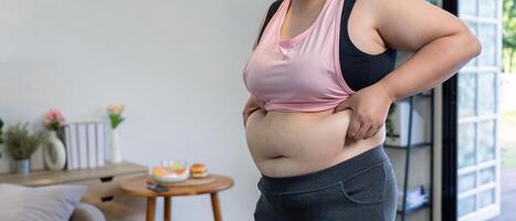 Woman assessing her waist while holding her stomach, contemplating body image in a comfortable living space photo