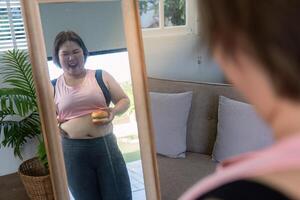 Confident woman holding a burger while laughing at her reflection, embracing body image positivity during her journey photo