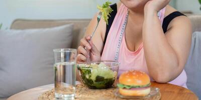 Mindful overweight woman choosing a healthy salad over a tempting burger, focusing on her weight loss journey photo