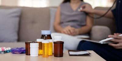 Caregiver performing health check-up on elderly client, surrounded by medication during consultation photo