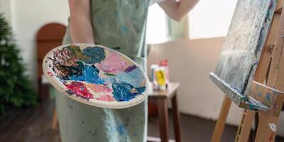 Focused artist presenting a colorful palette while preparing to paint on canvas in a light filled studio photo