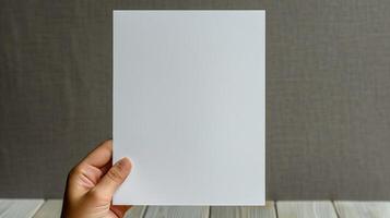 A hand holds a blank white sheet of paper against a textured gray backdrop photo