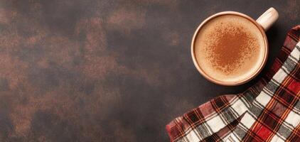 warm cappuccino in rustic ceramic cup rests on textured surface, accompanied by cozy plaid napkin, evoking sense of comfort and relaxation photo