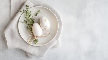Decorative white eggs on a plate with herbs and a ribbon showcased on a light textured surface photo