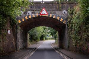 Low brick railway bridge over narrow road with height restriction sign photo