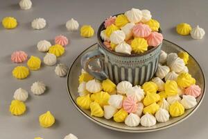 Multicolored meringue cake on a plate, in a mug, scattered on the table photo
