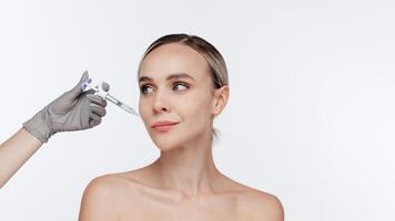 Blond woman receiving hyaluronic acid injection isolated on white background. Beautician doing beauty procedure to female face with syringe, injection to her cheek. Anti Aging Biorevitalization ads photo