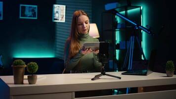 Influencer assessing portable speaker performance, talking about parts used, filming with phone. Girl recording music device review using smartphone on tripod, pleased with used materials, camera B video