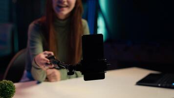 Close up of phone on selfie stick used by girl in apartment to capture intro for vlogging channel. Focus on smartphone used by entertainer in blurry background to film during live stream, camera A video