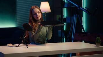 Young entertainer presenting sleek laptop from brand sponsoring , urging viewers to purchase it. Girl does influencer marketing by advertising thin notebook to audience in studio, camera A video