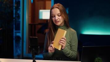 Young content creator films review of book, browsing through pages, presenting synopsis to audience. Internet star sponsored by publisher to show new novel release to readers, camera A video