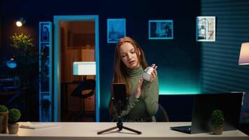 Gen Z girl in apartment studio using mobile phone to record, reviewing mini RGB lights. Young entertainer films electronics haul with cellphone on tripod, presenting LED lighting device, camera B video