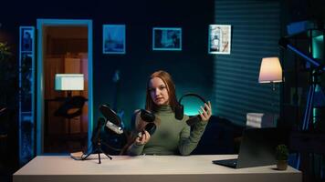 Gen Z influencer in home studio films headphones comparison for audience, recording with professional microphone to accurately capture sound, hosting technology internet show for fans, camera B video