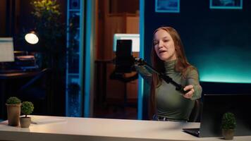 Gen Z teenager recording introductory with cellphone on selfie stick, inviting viewers to subscribe to channel. Influencer in home studio uses selfie camera to film herself, camera A video