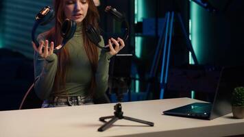 Internet show host holding pair of expensive headphones in hands, doing giveaway for loyal viewers, filming with phone. Girl hosting online contest for fans with audio tech as prize, camera A video