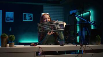 Gen Z girl presenting RGB lit mouse and keyboard while doing review in personal studio to see if price is justified. Young influencer showcasing neon lit computer peripheral features to fans, camera B video