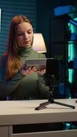 Vertical Influencer assessing portable speaker performance, talking about parts used, filming with phone. Girl recording music device review using smartphone on tripod, pleased with used materials, camera B video