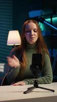 Vertical Smiling girl using smartphone on tripod to film herself discussing topics of interest for generation Z fanbase. Influencer recording targeting gen Z viewers using phone selfie camera, camera B video