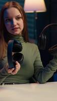 Vertical Gen Z influencer in home studio films headphones comparison for audience, recording with professional microphone to accurately capture sound, hosting technology internet show for fans, camera A video