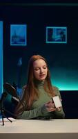 Vertical Cheerful gen Z girl in home studio reviewing mini RGB lights controller, using microphone to record. Smiling influencer films electronics haul, presenting LED lighting device, camera B video
