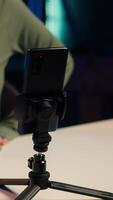 Vertical Focus on mobile phone used by influencer to film content for her online fans, talking about gen Z topics. Content creator records vlog for internet channel with cellphone on tripod, camera A close up video