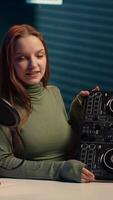 Vertical Cheerful girl mixing on DJ turntables, doing music production tutorial for online streaming channel. Smiling young content creator playing around with stereo sound mixer, camera A video