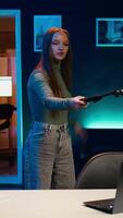 Vertical Happy gen Z girl recording introductory with smartphone on selfie stick, inviting viewers to subscribe to channel. Influencer uses selfie camera to film herself connecting with fanbase video