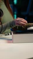 Vertical Gen Z content creator filming technology review of newly released smartphone, unpacking it and presenting specifications to audience. Internet star showing cellphone to fans from studio, camera A video