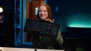 Gen Z girl presenting RGB lit mouse and keyboard while doing review in personal studio to see if price is justified. Young influencer showcasing neon lit computer peripheral features to fans, camera A video