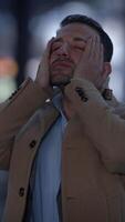 A man wearing a coat is displaying an emotional expression while being outdoors in a city video