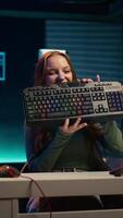 Vertical Gen Z girl presenting RGB lit mouse and keyboard while doing review in personal studio to see if price is justified. Young influencer showcasing neon lit computer peripheral features to fans, camera B video