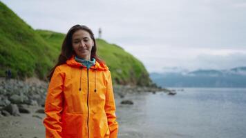 Portrait Of Happy Woman Tourist In Orange Raincoat In Landscape With Picturesque Cape With Greenery video