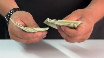 Hands carefully sort through a stack of dollar bills at a table, focused on counting money for an upcoming financial transaction, ensuring accuracy video