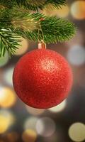 Vertical close-up of a red Christmas ornament on a tree with bokeh lights in the background, featuring space for promotional text or a logo photo