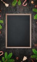 Chalkboard centered on a table surrounded by Christmas tree branches and decorations, featuring an empty surface for writing promotional text in a festive setting photo