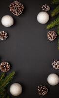 Top view flat lay of Christmas decorations on a black background, surrounded by white ornaments, fir branches, and pinecones, featuring central space for text or logo photo