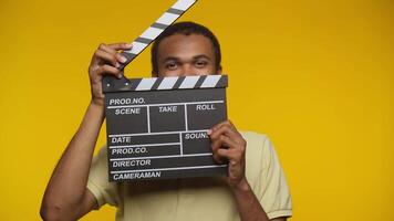 Young Man Holding Clapperboard with Playful Expression Against Yellow Background video