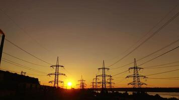Sunset among high voltage towers. Transmission lines on the setting sun background. Electricity distribution in the evening. Motion camera back. video