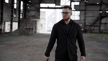 Handsome man in ruined place. Serious bearded man in glasses stands with baseball bat inside the damaged building. Camera moves in around. video