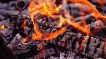 Coals are burning in the fire. Smoldered logs with slight flame background. Fire transforms the wood into charcoal. Close-up. Slow motion video