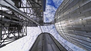 Innovative factory. Huge grain elevators on beautiful sky background. Modern plant. Close-up. View from below. Motion camera in a round way. video