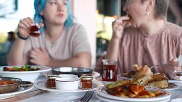 two women are laughing and talking as they eat, clearly enjoying each other's company. Turkish Breakfast, Sunday breakfast or brunch with feta cheese and eggs, Turkish meal served in restaurant video