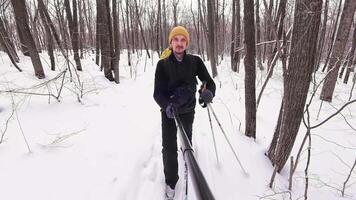 An individual skis through a serene snowy forest, surrounded by tall trees and fluffy snow. Dressed in warm gear and a cheerful yellow hat, they enjoy the winter sports experience video